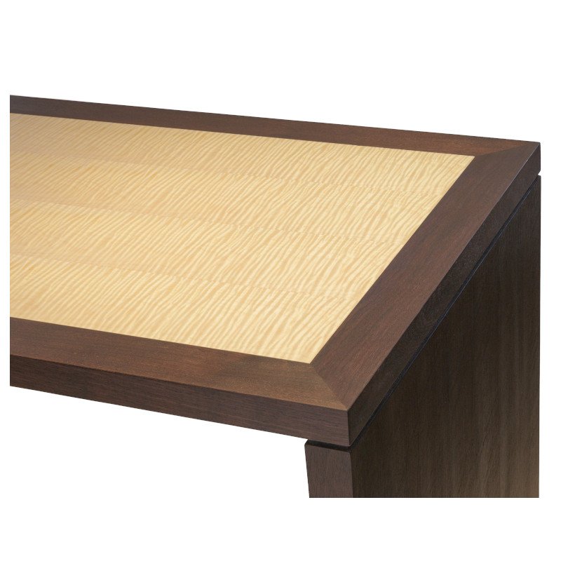 Close-up of a wooden desk top with a light-colored curly maple top and dark-colored frame.
