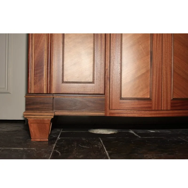 Close-up of wooden vanity cabinet with a decorative leg, and dark tiled floor.