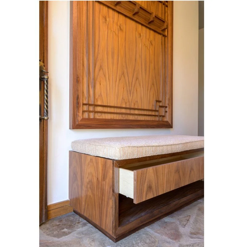 A wooden entryway bench with a cushioned seat and a large wooden wall panel with a geometric pattern.
