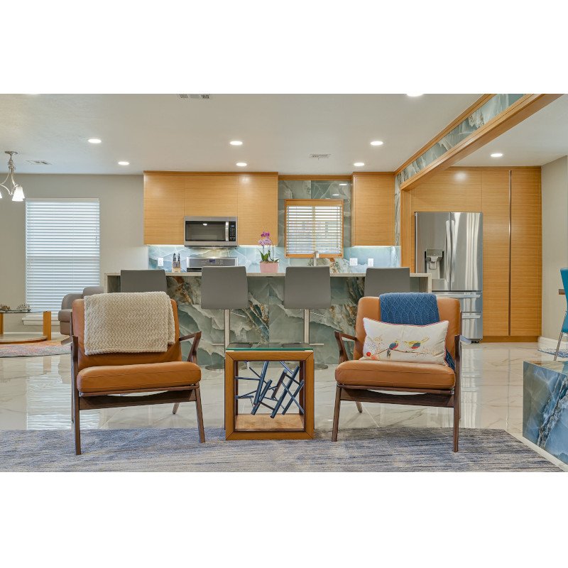 Living room area with two orange armchairs, a small wooden side table, and a marble kitchen island in the background.