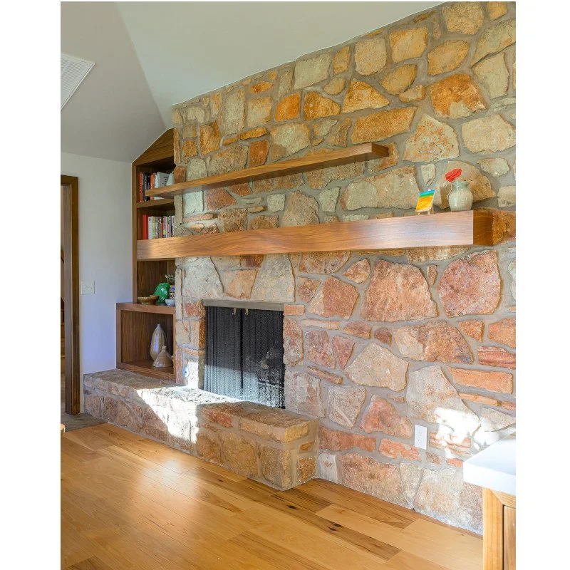 Interior view of a living room with a stone fireplace, wooden shelves, and hardwood flooring.