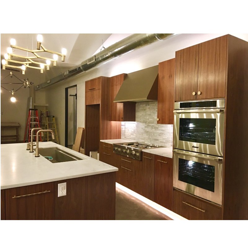 Modern kitchen with wood cabinetry, stainless steel double oven, and a white marble countertop island with a built-in sink.