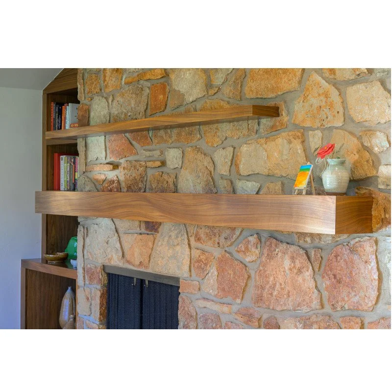 Wooden shelves mounted on a stone fireplace wall, with decorative items like a vase with a flower and a small colorful object on the top shelf, and books on the side bookshelf.