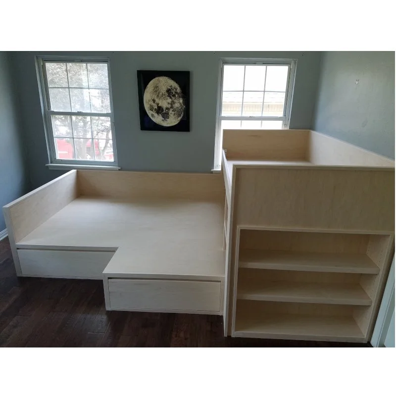 Empty unfinished wooden bed frame with built-in storage and shelves in a room with two windows and a moon poster on the wall.