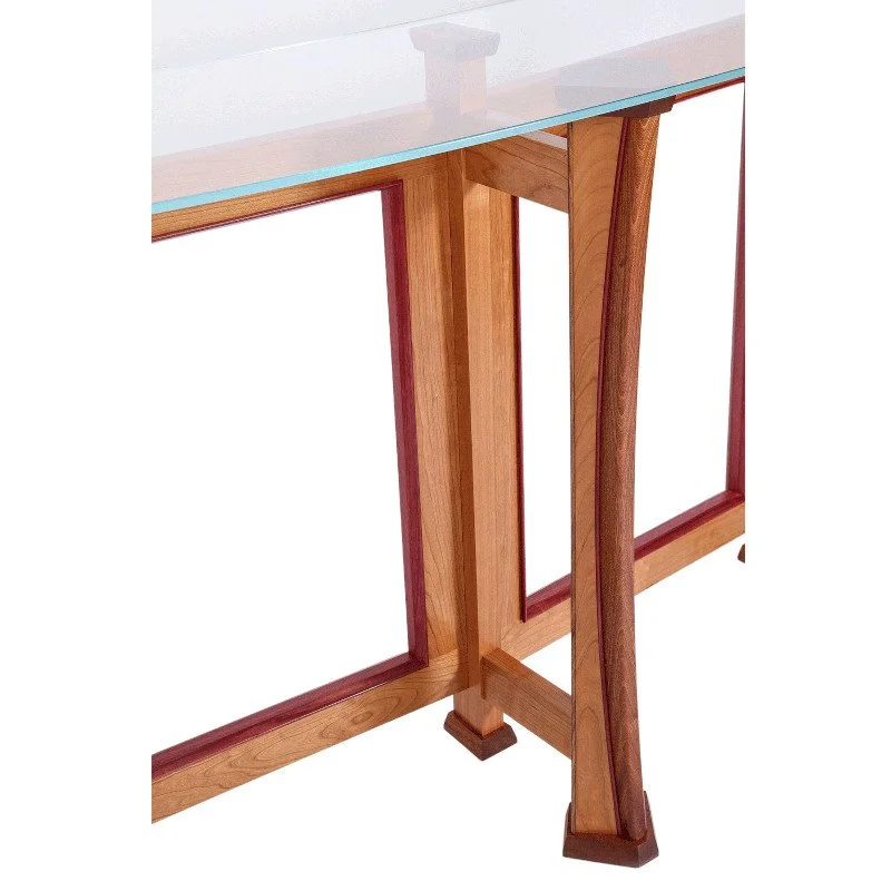 Close-up of a wooden table with a glass top, showcasing the detailed craftsmanship and joinery of the table's legs and frame.