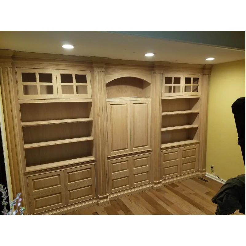 Wooden built-in bookshelf unit with shelves and cabinet doors in a room with hardwood floors and yellow walls.