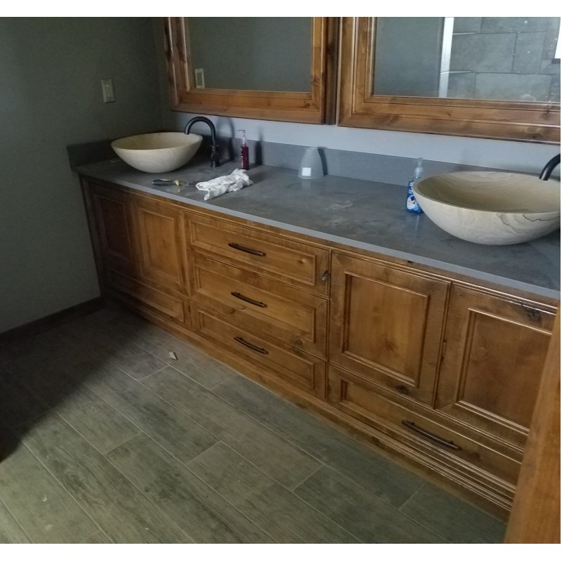 Bathroom vanity with wooden cabinets, two vessel sinks, mirrors above, and various toiletries on the gray countertop.