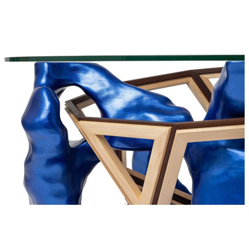 Close-up of a modern glass-top table with a blue sculpture that has a glossy finish and an intricate wooden frame.