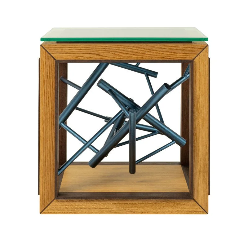 A wooden side table with a glass top, containing an abstract metallic painted sculpture inside.