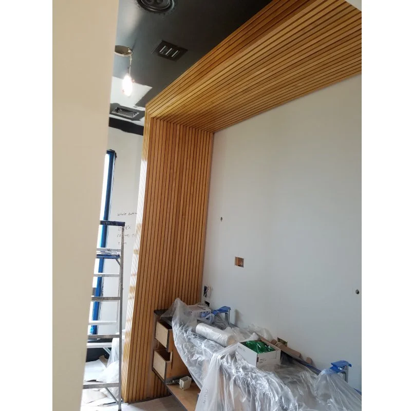 Interior of a bathroom under construction with modern wood fluting on the wall extending to the ceiling, construction materials, and tools on a covered surface, a ladder, and partially installed electrical outlets.
