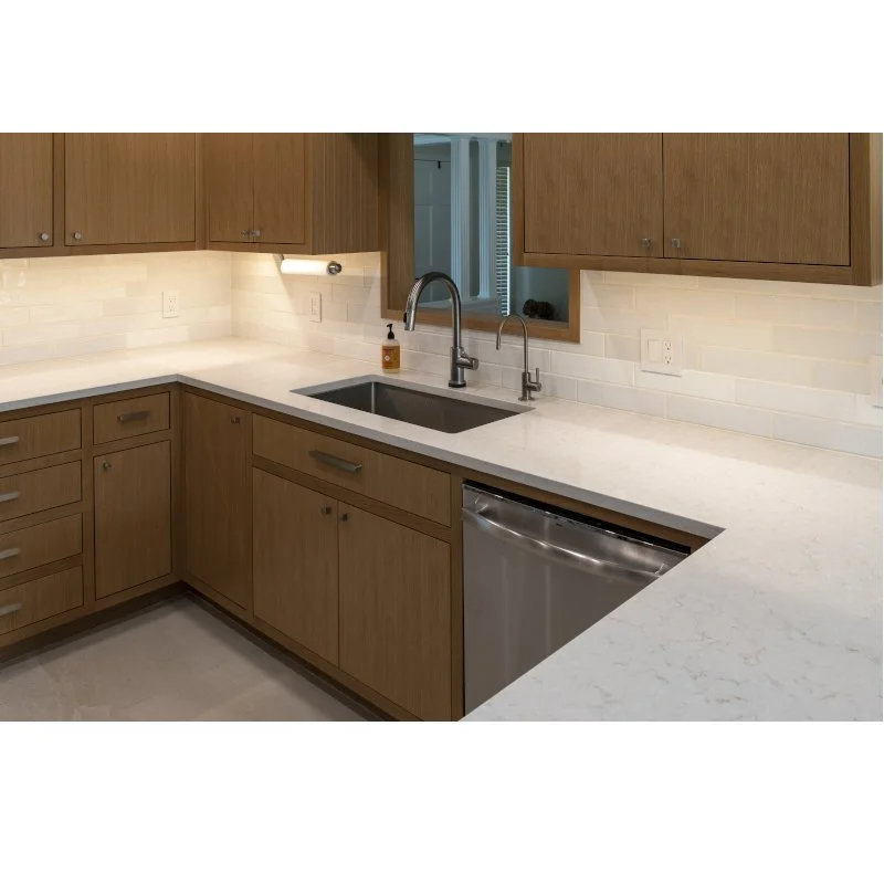 Modern kitchen with wooden cabinets, white countertop, stainless steel sink, faucet, soap dispenser, under-cabinet lighting, and a dishwasher.