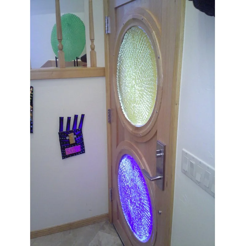 A wooden door with two circle art glass panels, back lit with sun light, in an indoor setting.