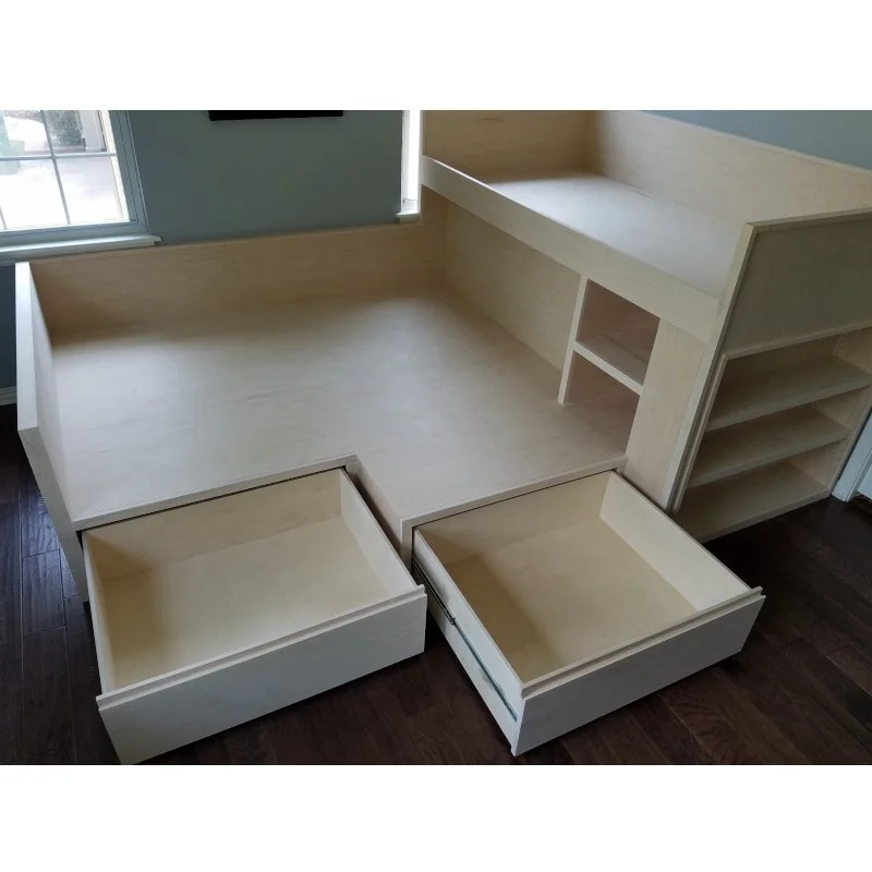 Unfinished wooden bed with built-in storage drawers and shelves, placed in a room with hardwood floors and a window.