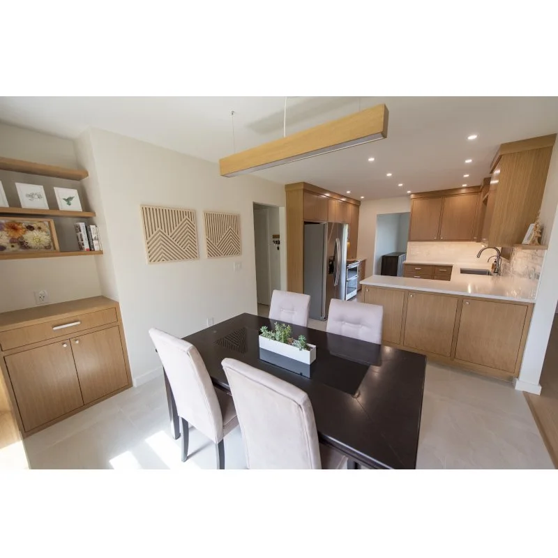 Dining area with a dark wood table, four beige upholstered chairs, and modern decor. Open kitchen with wood cabinets, stainless steel refrigerator, and a white countertop.