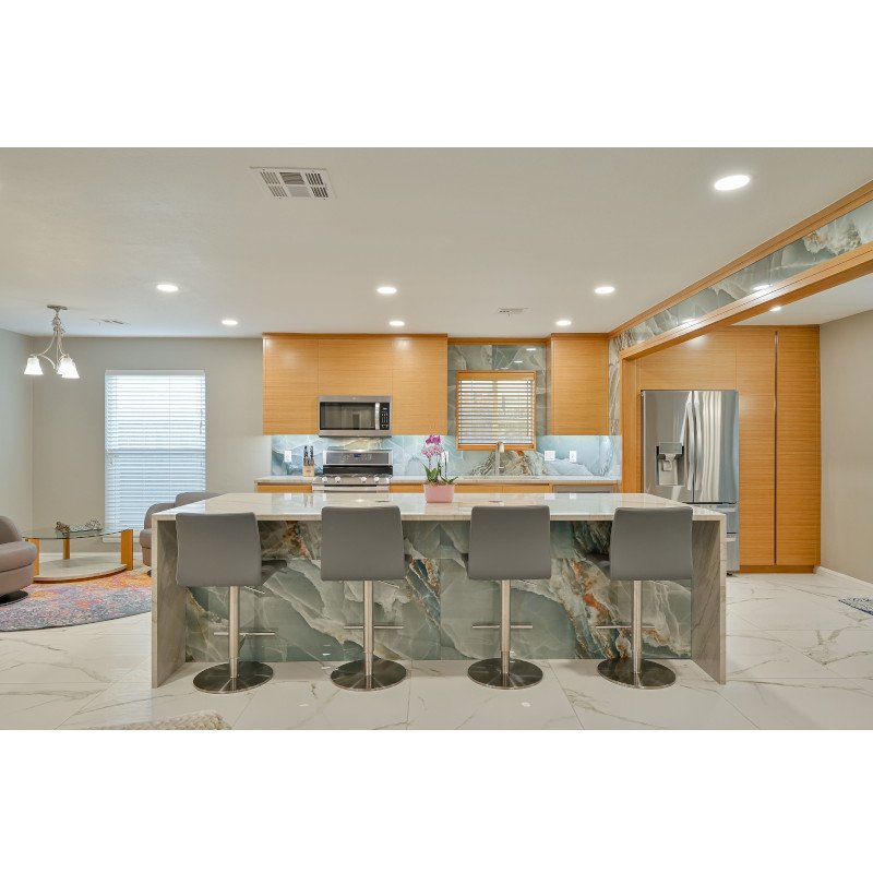 Modern kitchen with marble island, wooden cabinets, stainless steel appliances, and gray bar stools.