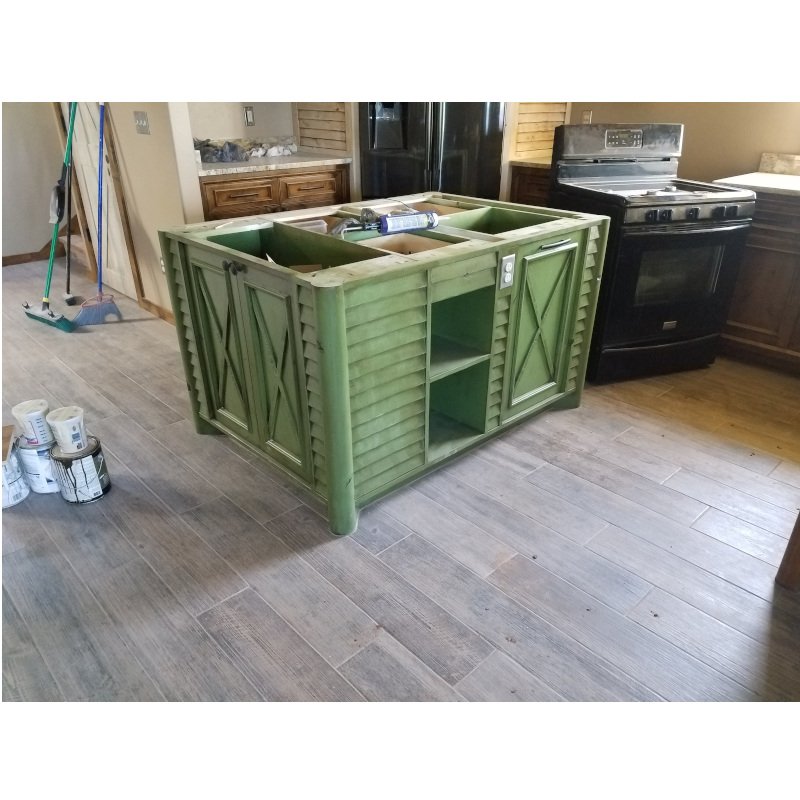 A kitchen with a black stove, wooden cabinets, and a partially painted green island under construction.