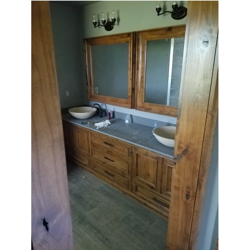 A bathroom vanity with wooden cabinets and a gray countertop, featuring two round vessel sinks, mirrors above each sink, and a light fixture with multiple bulbs on the ceiling.