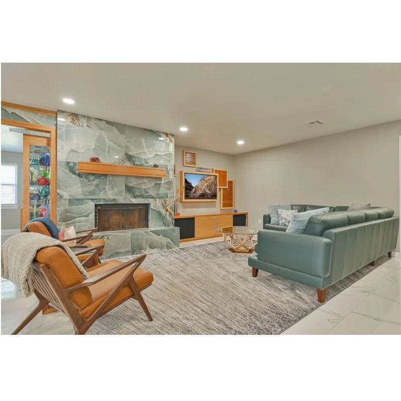 Modern living room with a green couch, wooden chairs, a fireplace with a marble surround, and a television on a wooden media console.