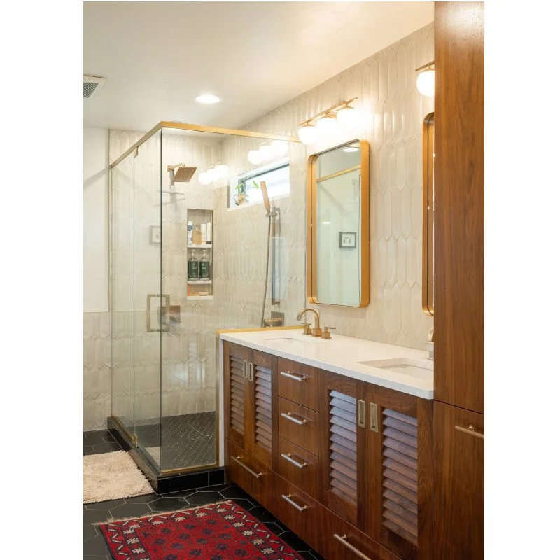 Bathroom with wooden vanity, rectangular mirror, glass shower enclosure, and black tile flooring.
