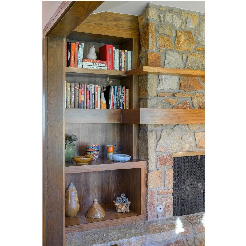 Wooden and stone built bookshelf with books, decorative vases, bowls, and a jar displayed.