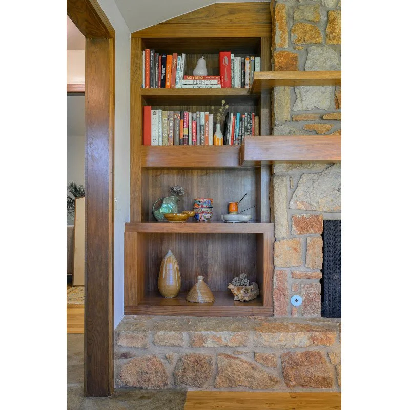 Built-in wooden bookshelf next to a stone fireplace with decorative vases and books.
