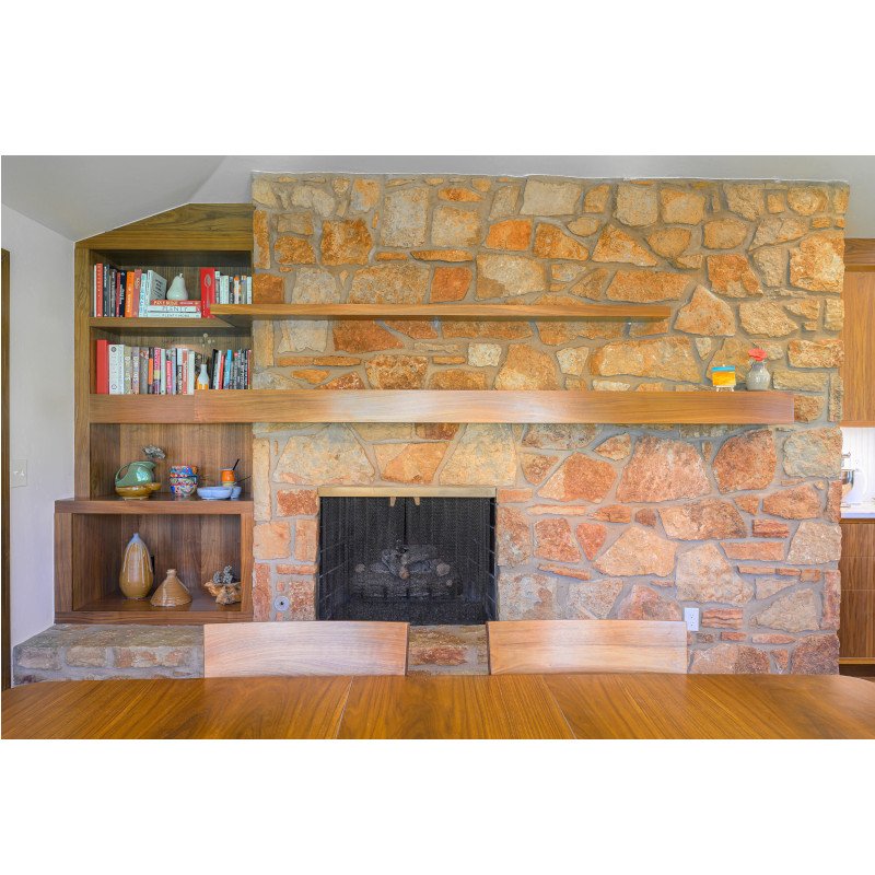 Interior view of a living room fireplace with a stone wall and wooden shelves holding books and decorative items.