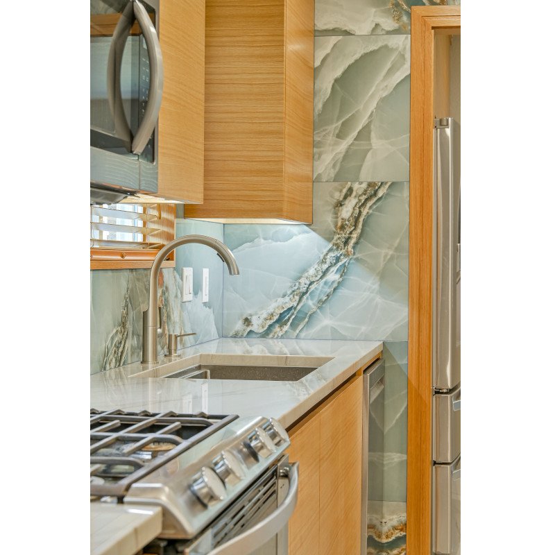 Modern kitchen with white oak cabinets, quartzite countertops, and a marble backsplash with green, white, and gold veins. Includes a stainless steel microwave, stove, and refrigerator.