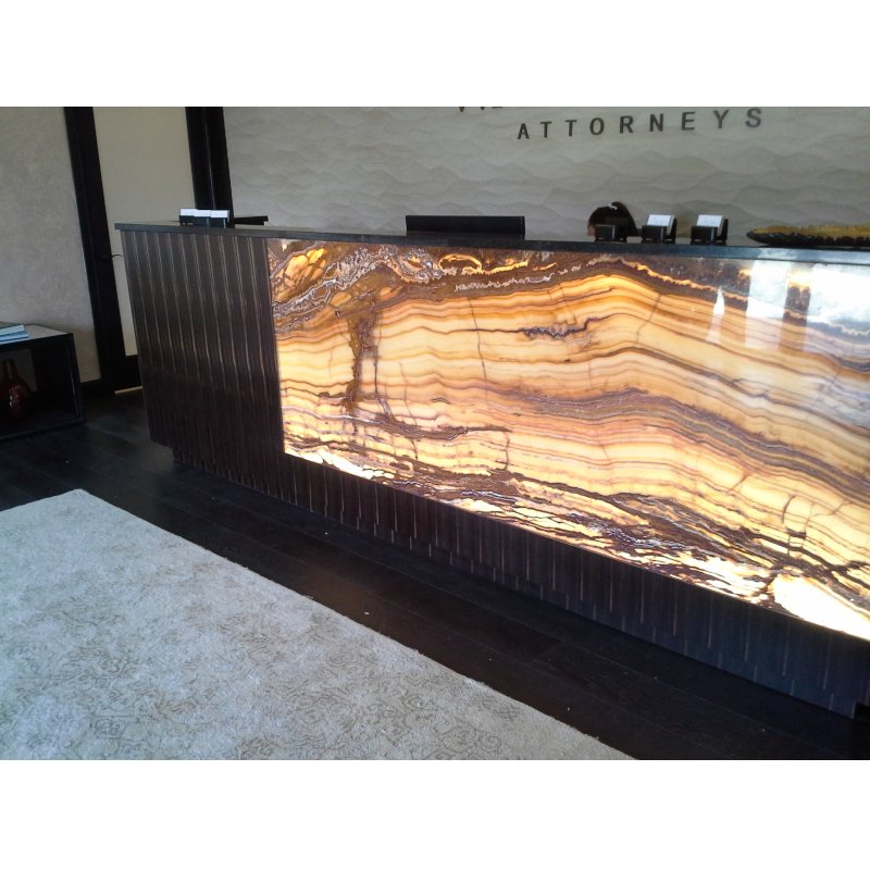 Reception desk with a backlit onyx stone front and black vertical striped sides in an attorney's office.