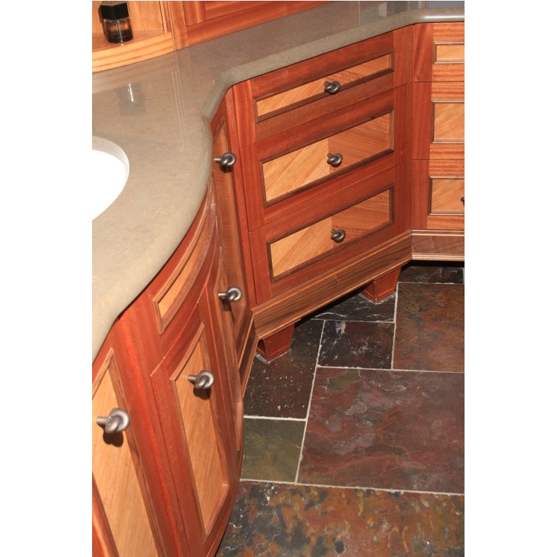 Close-up view of a wooden bathroom vanity with drawers and cabinet doors, a light-colored countertop, and multicolored stone tile flooring.