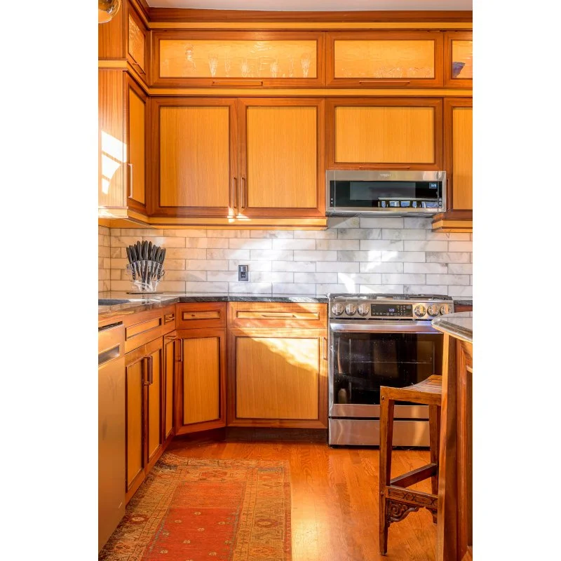 Kitchen with wooden cabinets, stainless steel microwave and oven, tile backsplash, countertop, knife holder, and a small rug.