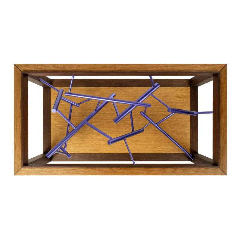 An artistic sculpture metallic painted dowel rods placed inside a wooden framed coffee table.