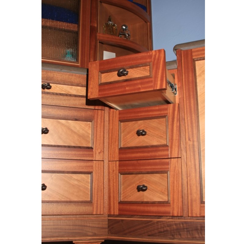 A section of wooden kitchen cabinets with multiple drawers and an open small drawer. The cabinets are made of wood with a natural finish, and some decorative items are visible on the shelves above.