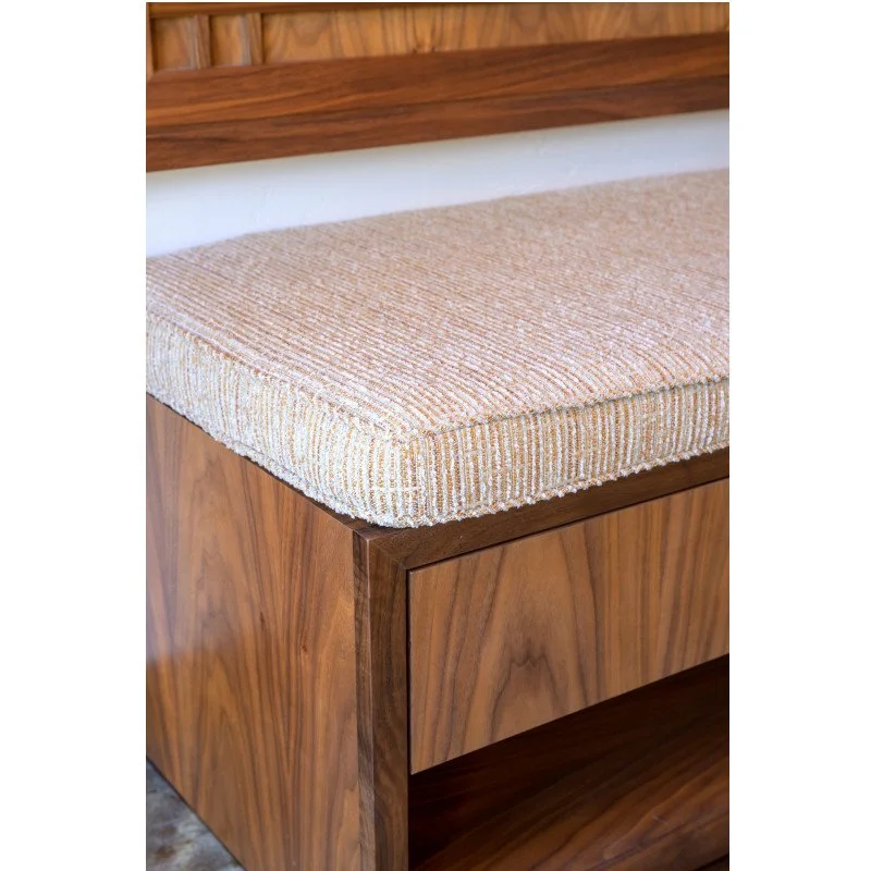Close-up of a wooden bench with a beige upholstered cushion on top.