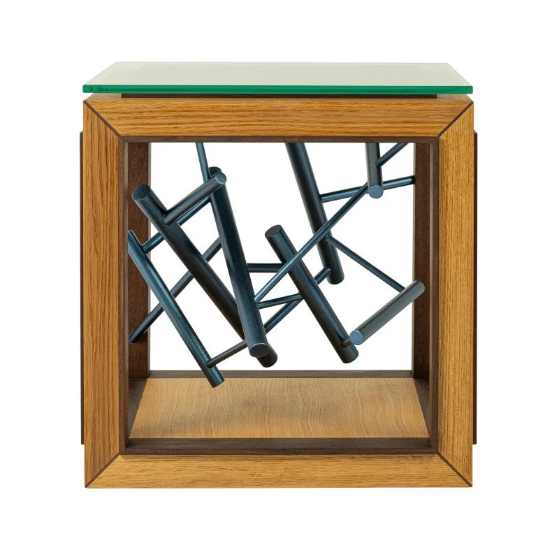 A wooden side table with a glass top and a cube-shaped open frame, containing dowel rods arranged in a chaotic manner and painted with metallic paint.