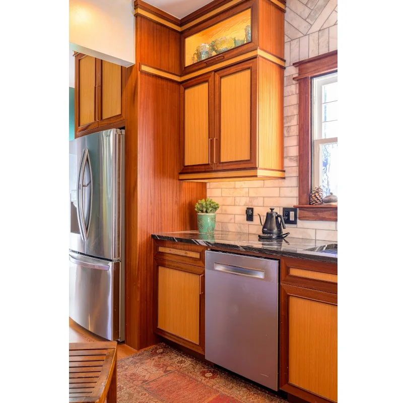 Kitchen corner with wooden cabinets, a stainless steel refrigerator, and a window with wood trim.