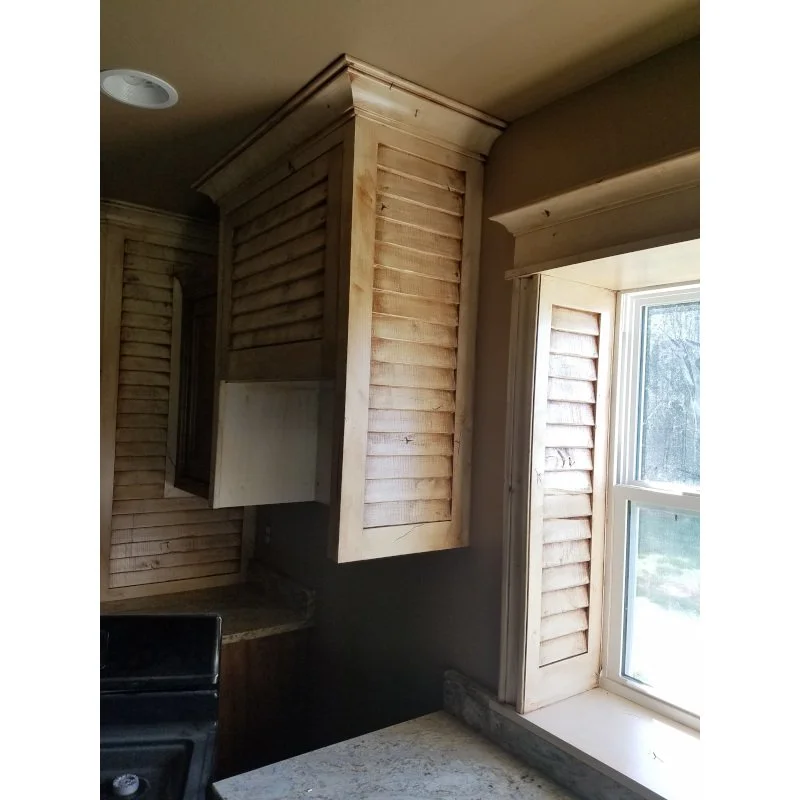 Wooden kitchen cabinet with ship lap trim next to a window with a beige frame and a view outside.