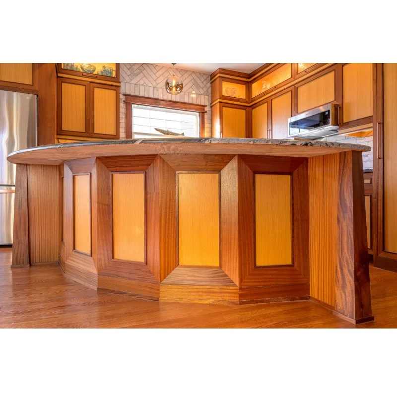 Close-up of a wooden kitchen island with a granite countertop, surrounded by wooden cabinetry and a window in the background.