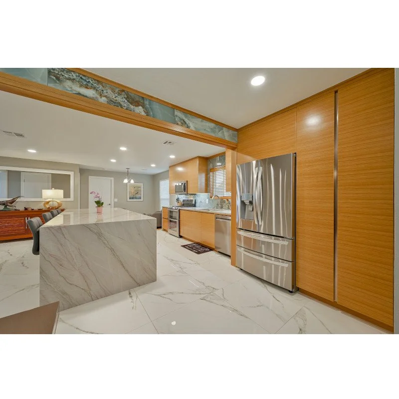 Modern kitchen with wooden cabinets, stainless steel refrigerator, quartzite island with waterfall ends, and marble flooring.