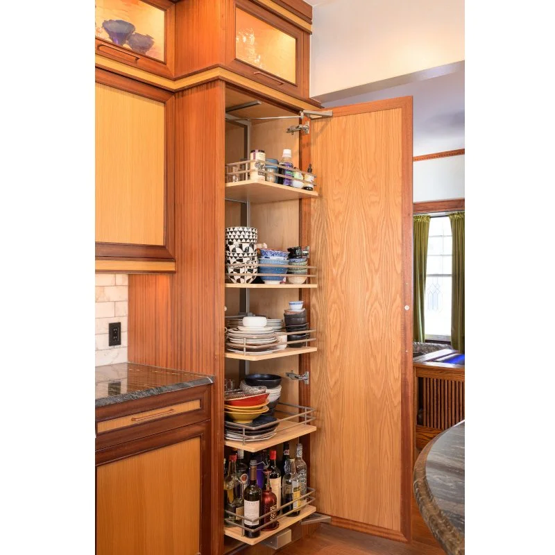 Open wooden kitchen cabinet with multiple shelves filled with dishes, bowls, and bottles, next to a countertop with a granite surface.