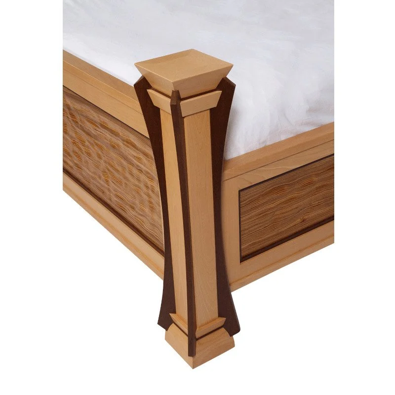 Close-up of a wooden bedpost with decorative dark wood accents and a tan finish, part of a bedroom bed frame.