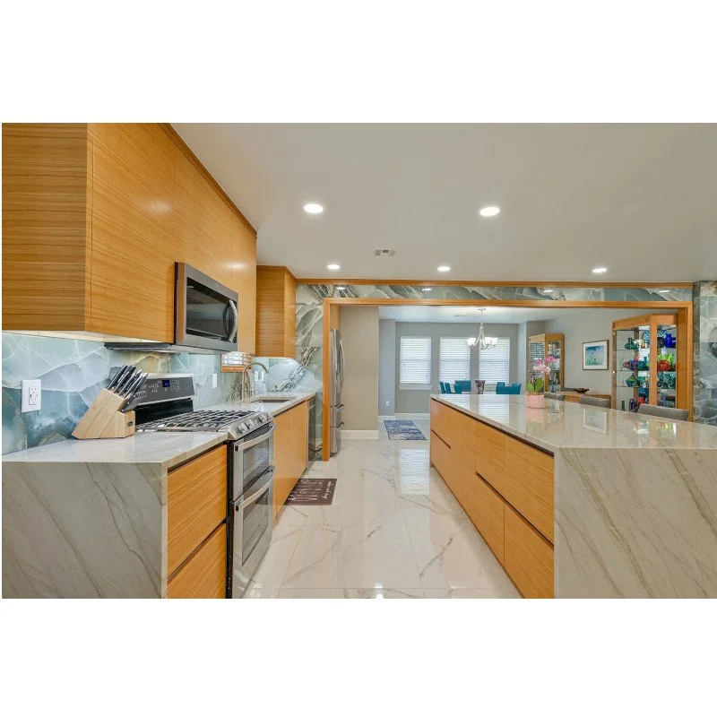 Modern kitchen with wooden cabinets, marble countertops, stainless steel appliances, and a view into the dining and living area.