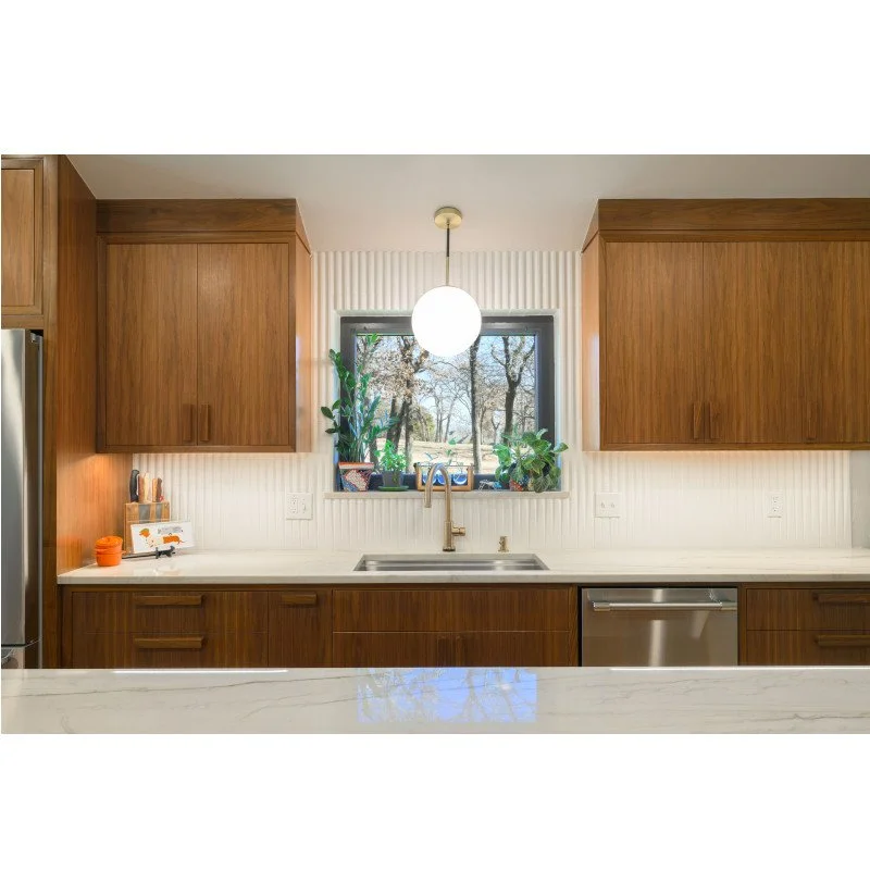 Modern kitchen with wooden cabinets, white countertop, stainless steel dishwasher, and a window with plants and trees outside.