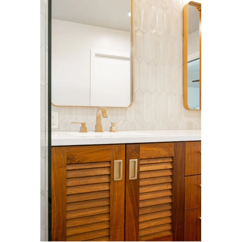 Bathroom vanity with a wooden cabinet, a white countertop, a gold faucet, and two mirrors on the wall.