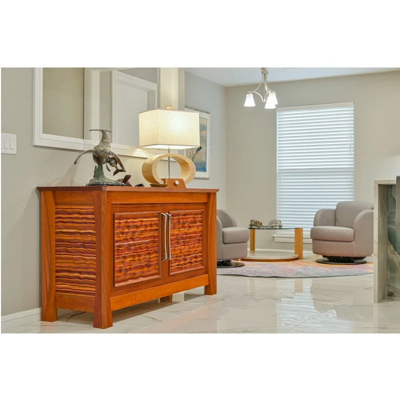 Living room with a wooden sideboard, a lamp, artwork, two beige chairs, a window with blinds, a round coffee table, and a patterned rug.