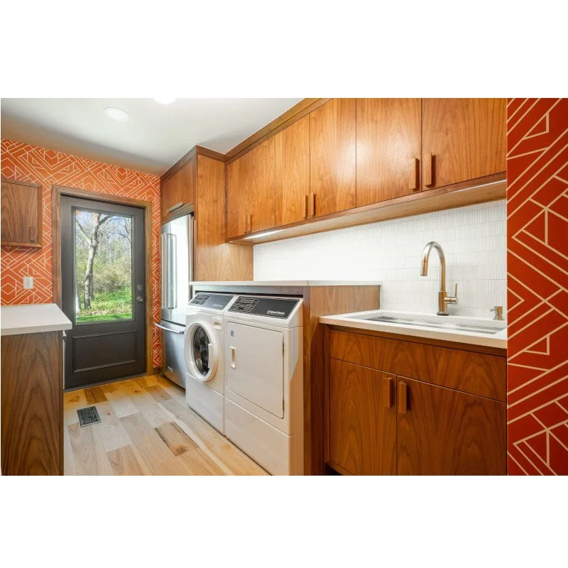 Laundry room with wooden cabinets, a washing machine, a dryer, a white countertop with a sink, and a door leading outside.