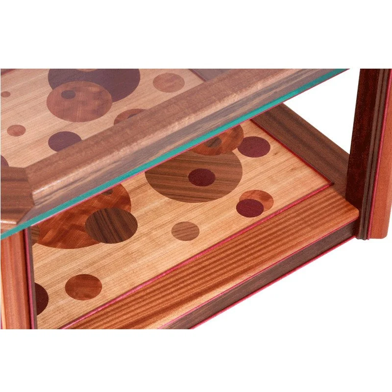 Close-up of a wooden coffee table with a glass top and a patterned wooden floor with circular designs.