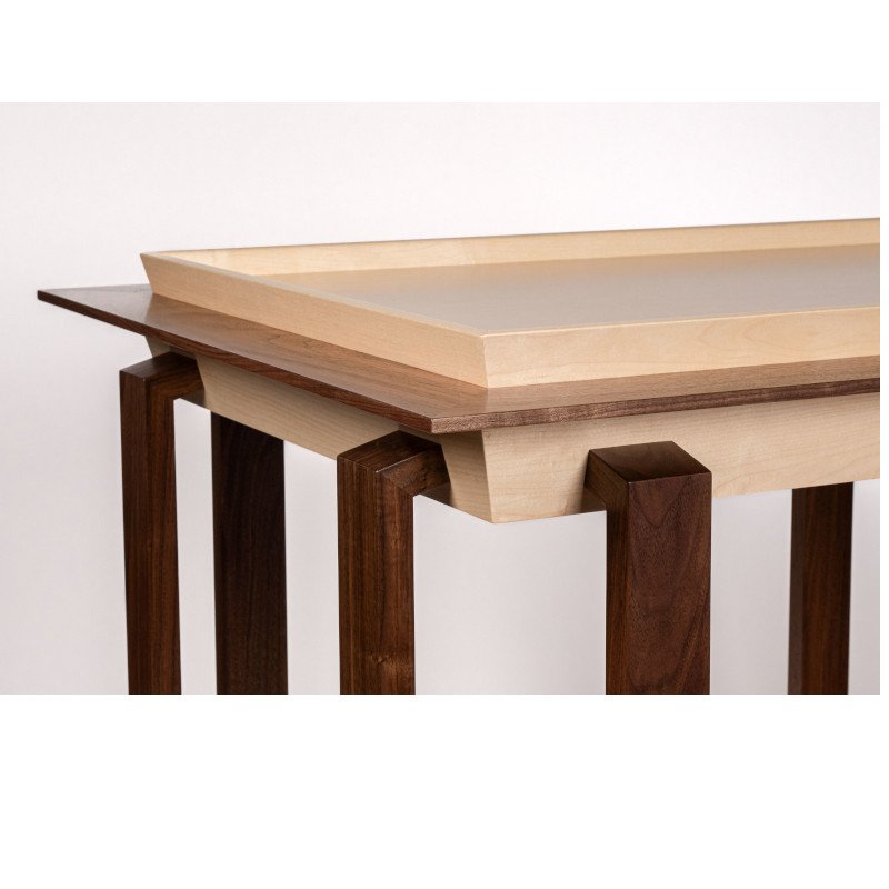 Close-up of a modern wooden table with a layered tabletop design, featuring light and dark wood, against a plain white background.