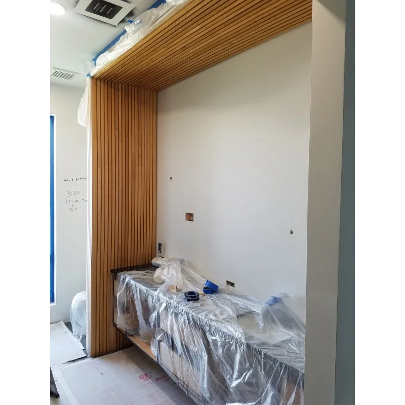 Construction area with wood paneling on the wall and ceiling, covered in protective plastic sheeting. There are construction tools and supplies on a covered surface.