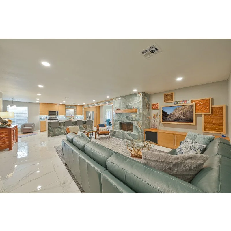 Spacious living room with green sectional couch, stone fireplace, and modern decor, opening to a kitchen area with quartzite countertops.