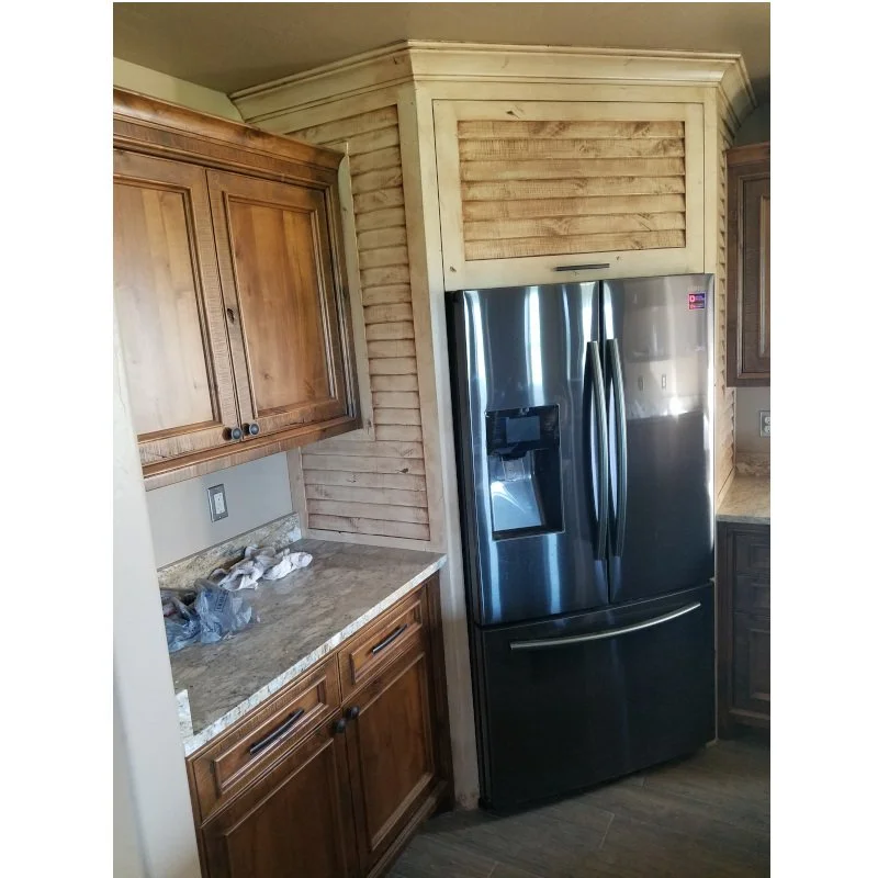 Kitchen corner with wooden cabinets, a marble countertop, and a stainless steel refrigerator surrounded by wood paneling.